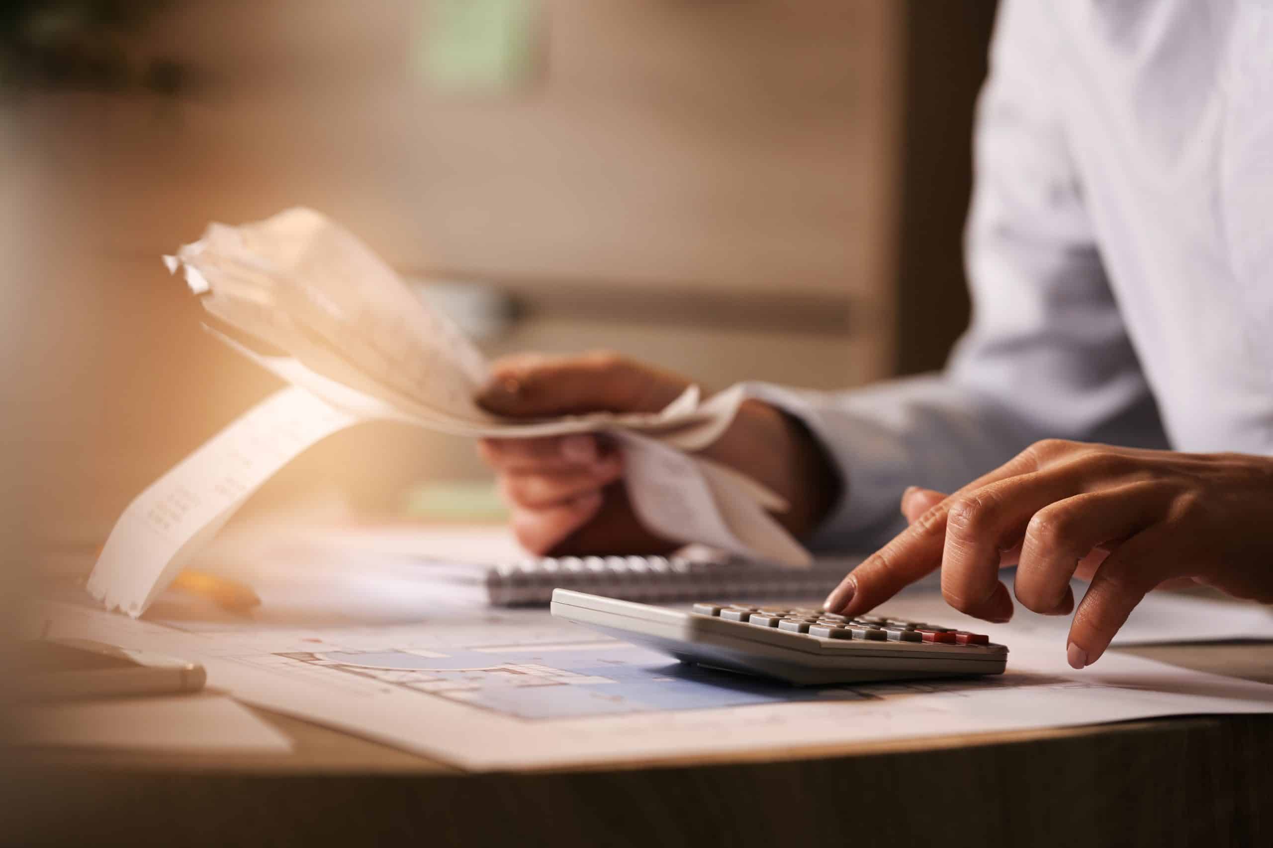 Closeup Economist Using Calculator While Going Through Bills Taxes Office Scaled 1